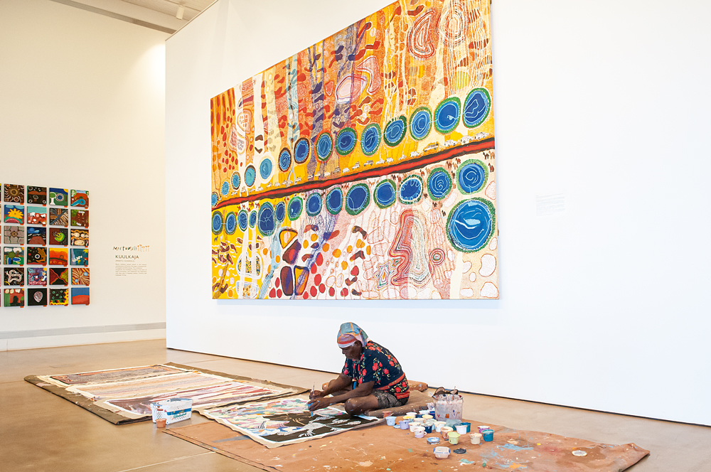 Ngamaru Bidu paints beneath the Our Country canvas. Ngamaru is a member of Martumili Artists, an Aboriginal art group representing remote Indigenous communities, which is showcased in the East Pilbara Arts Centre in Newman, WA. Photo by Mandy McKeesick. Art OUTBACK #Issue 132.